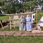 Vanessa Coombs - Traditional Wool Spinning and Historic Embroidery Two ladies dressed in old style clothing at wool spinning equipment